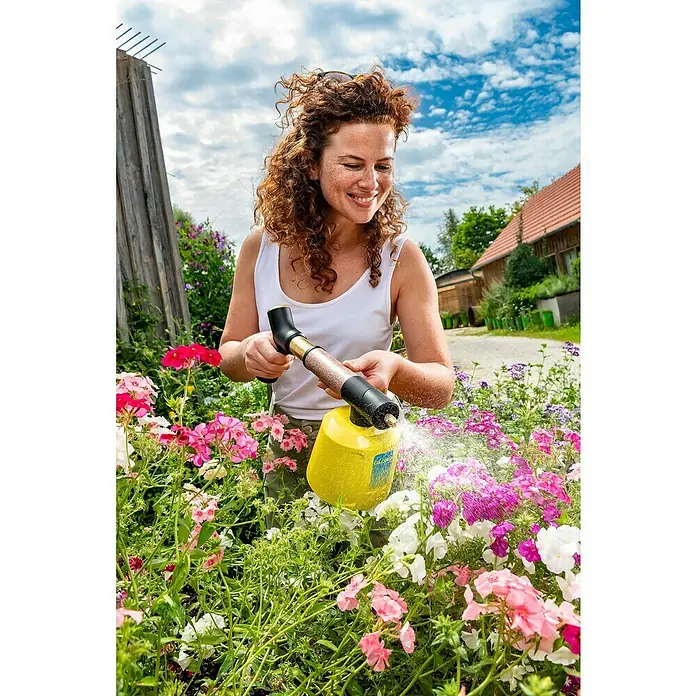 Gloria Akku-Feinsprüher Hydronette li-on - 3,6 V, 1 Akku - Eine Frau gießt Blumen mit einem Gloria Sprühgerät, umgeben von blühenden Blumen in einem Garten mit blauem Himmel im Hintergrund.