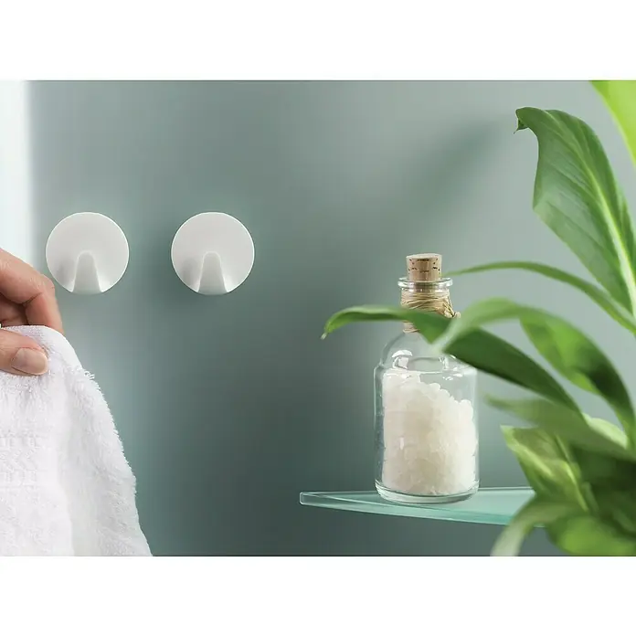 Tesa Powerstrips Selbstklebehaken - Rund, Größe: S, Weiß, 3 Stk. - Nahaufnahme von zwei weißen Wandhaken, einem Handtuch und einer Glasflasche mit Badesalz auf einem Regal.