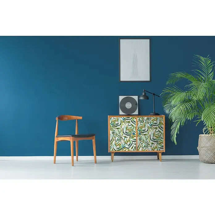 D-c-fix Lámina para ventana Lorina - 45 x 200 cm, Verde/Amarillo/Gris - Interior con un armario con estampado de hojas, una silla, una planta de interior, una lámpara, un disco y una imagen enmarcada en la pared.