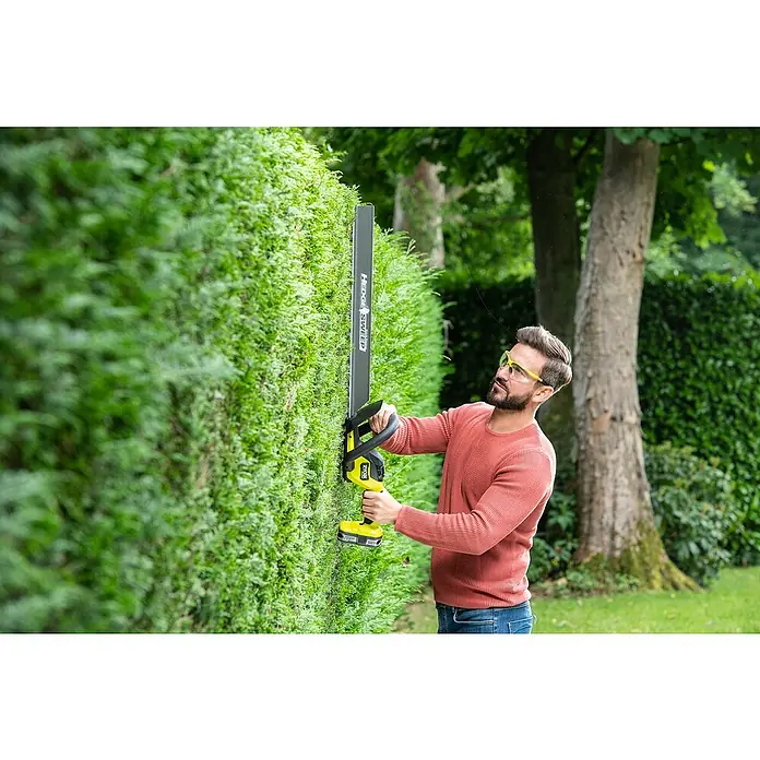 Ryobi ONE+ Maschinenpaket - Akku-Heckenschere RY18HTX60A-0,18V, 4 Ah Akku & 2A Ladegerät - Ein Mann schneidet eine Hecke mit einer Ryobi Heckenschere, wobei der Fokus auf der Präzision und Benutzerfreundlichkeit des Geräts liegt.
