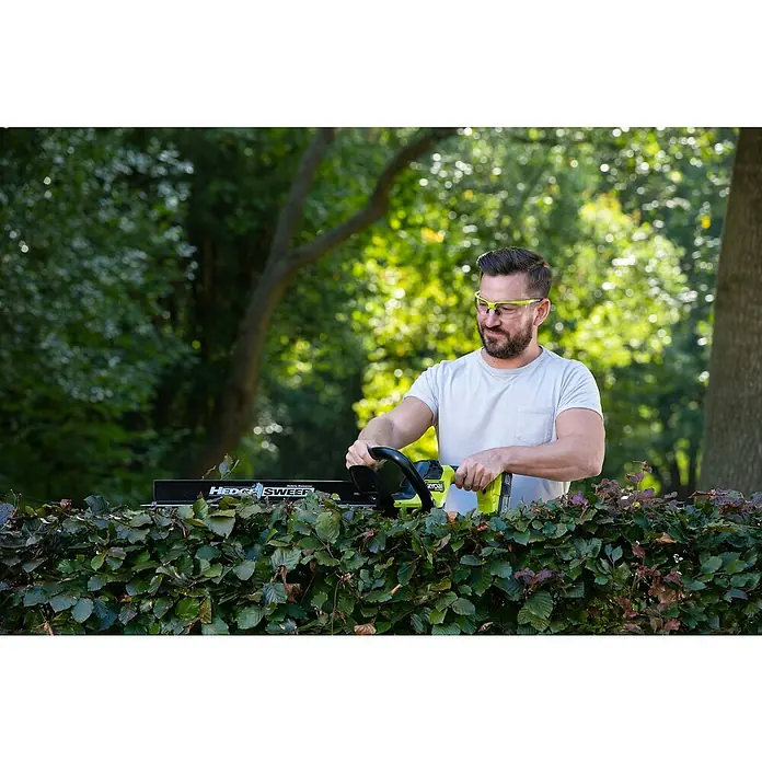 Ryobi ONE+ Maschinenpaket - Akku-Heckenschere RY18HTX60A-0,18V, 4 Ah Akku & 2A Ladegerät - Mann schneidet Hecke mit Ryobi Heckenschere und Schutzbrille in Garten.