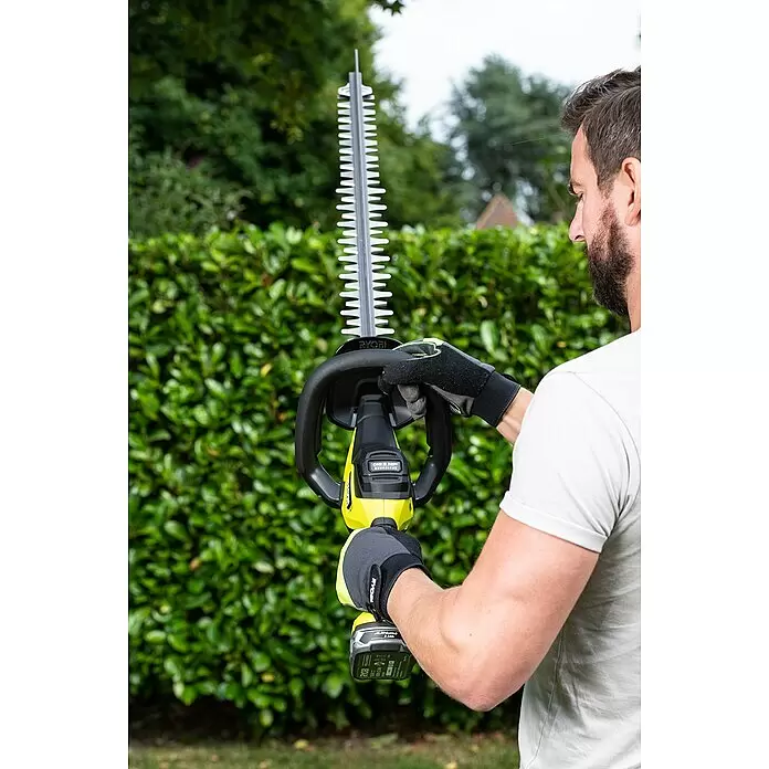 Ryobi ONE+ Akku-Heckenschere RY18HTX60A-0 - 18 V, Li-Ionen, Ohne Akku, Schwertlänge: 60 cm - Mann mit Handschuhen hält eine gelb-schwarze Ryobi Heckenschere zum Schneiden von Sträuchern.