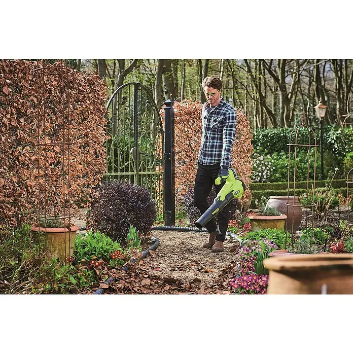 Ryobi ONE+HP Akku-Laubbläser RY18BLXC-0 - 18 V, Ohne Akku, Blasgeschwindigkeit: 177 km/h, Blasleistung: 9,9 m³/min - Ein Mann benutzt einen grünen RYOBI Akku-Laubbläser im Garten, um Laub zu entfernen, und trägt dabei Sicherheitsbrille.
