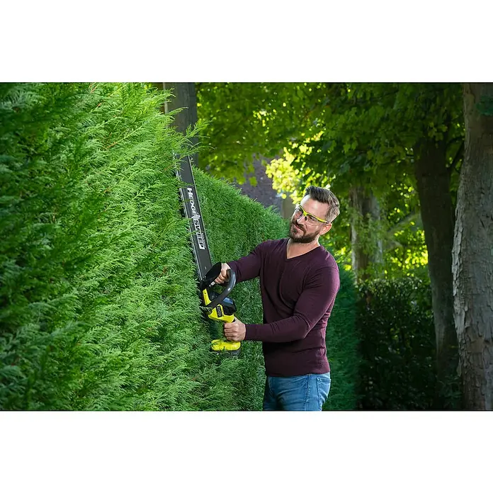 Ryobi ONE+ Akku-Heckenschere RY18HT55A-0 - 18 V, Li-Ionen, Ohne Akku, Schwertlänge: 55 cm - Mann, der eine Ryobi Heckenschere benutzt, um einen grünen Strauch zu schneiden. Die Heckenschere ist ein Hedge Sweep Modell mit gelbem Griff.
