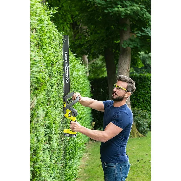 Ryobi ONE+ Akku-Heckenschere RY18HT55A-0 - 18 V, Li-Ionen, Ohne Akku, Schwertlänge: 55 cm - Ein Mann trimmt eine Hecke mit einer Ryobi Heckenschere, mit Fokus auf das Werkzeug und seine Anwendung.