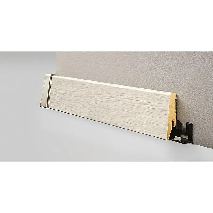 LOGOCLIC Sockelleiste K40 C Eiche Weiß - 260 cm x 19 mm x 40 mm, MDF - Eine weiße Holzfußleiste mit silberner Endkappe, die an einer grauen Wand befestigt ist. Die Leiste wird durch eine schwarze Halterung stabilisiert.