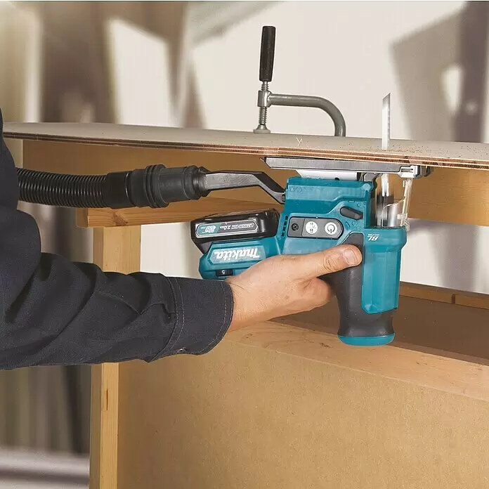 Makita CXT 12V max. Sierra de calar de batería JV102DZ - 12 V, Sin batería - Una mano opera una sierra de calar inalámbrica Makita turquesa y negra con extracción de polvo, cortando madera en un banco.