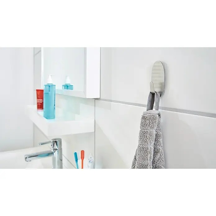Tesa Powerstrips Selbstklebehaken - Oval, Größe: L, Metallic, 1 Stk. - Ein graues Handtuch hängt an einem silbernen Wandhaken in einem modernen Badezimmer, das ein sauberes und minimalistisches Design aufweist.