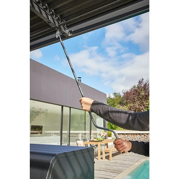 Sunfun Melina Grillpavillon - B x T: 250 x 160 cm, Farbe Gestell: Schwarz, Aluminium - Nahaufnahme einer Person, die mit einer Stange ein Lamellendach bedient, das sich über einer Terrasse mit modernen Möbeln befindet.