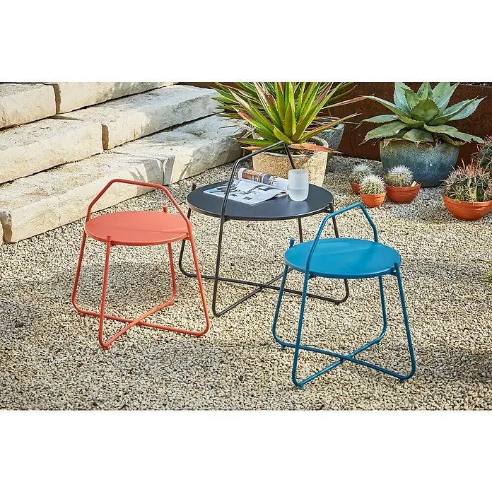 Sunfun Melina Garten-Beistelltisch rund - Ø x H: 80 x 60,5 cm, Stahl, Schwarz - Zwei moderne Stühle in Orange und Blau neben einem runden Tisch im Außenbereich, umgeben von Pflanzen und Kies.
