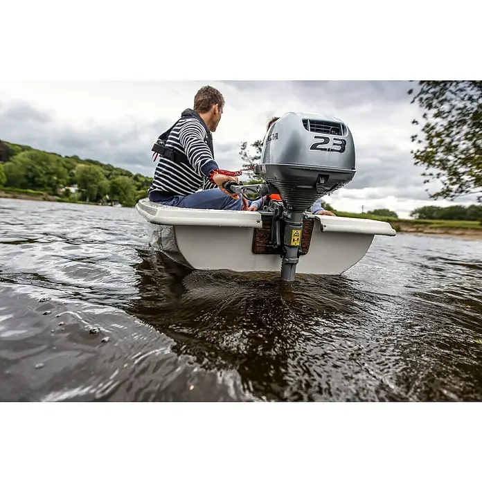 Honda Marine Außenbordmotor BF 2.3 SCHU - 1,7 kW, Pinnensteuerung, Kurzschaft, Seilzug - Mann steuert ein Boot mit einem silbernen 2,3-PS-Honda-Außenbordmotor auf einem Fluss. Der Motor dominiert das Bild mit seinem markanten Design.