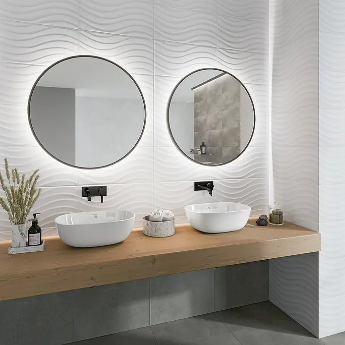 Ambiente by Palazzo Wandfliese Snowwhite Wave - 30 x 60 cm, Stärke: 9 mm, Weiß, Matt - Elegantes Badezimmerdesign mit zwei runden Spiegeln, modernen Waschbecken und einer stilvollen Holzablage vor einer Wand mit Wellenmusterfliesen.