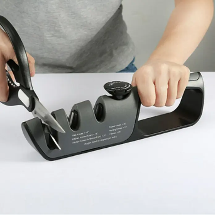 Afilador Premium - Específico para: Tijeras, cuchillos y navajas - Imagen de una persona afilando unas tijeras con un afilador de cuchillos que ofrece varios ángulos de afilado para cuchillos.