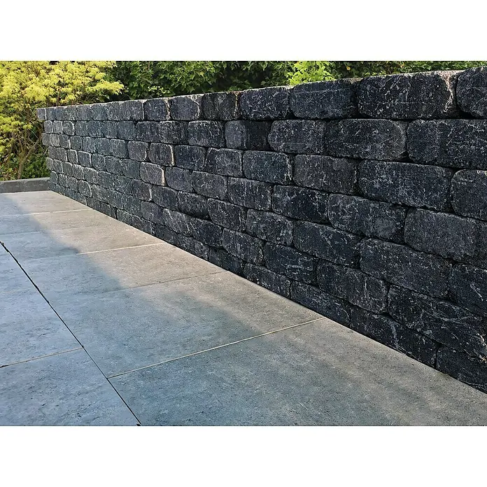 Diephaus Mauerstein Austin - 30 x 20 x 10 cm, Basalt, Beton - Bild einer massiven, dunklen Steinmauer, die einen modernen Gartenbereich ergänzt, mit eleganten Bodenplatten im Vordergrund.