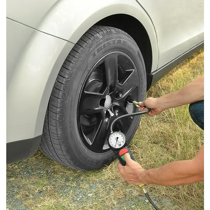 Craftomat Reifenfüllmesser PRO geeicht - Betriebsdruck: 0 bar - 10 bar - Nahaufnahme einer Person, die mit einem Reifendruckmesser den Reifendruck eines Autos misst.