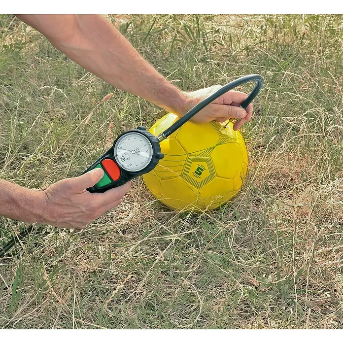 Craftomat Reifenfüllmesser PRO geeicht - Betriebsdruck: 0 bar - 10 bar - Nahaufnahme von Händen, die einen gelben Fußball auf einem Rasen mit einem Reifendruckmesser überprüfen.