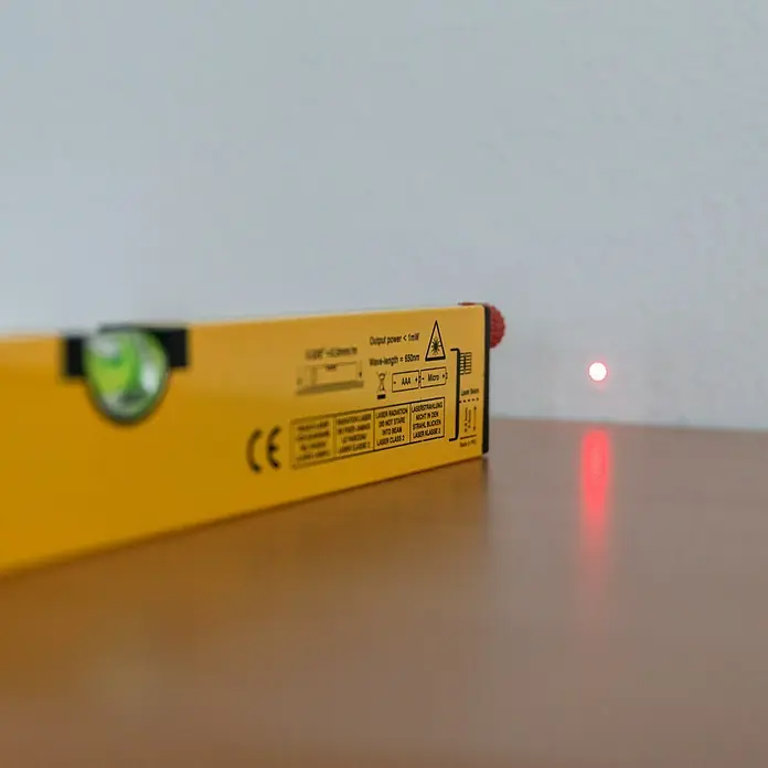 Wisent Werkzeugkoffer Professional - 160 -tlg. - Nahaufnahme einer gelben Laser-Wasserwaage, die einen roten Laserpunkt auf eine Oberfläche projiziert.