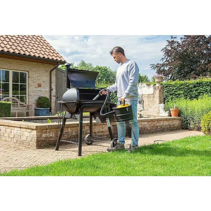 PowerPlus Aspirador de cenizas eléctrico POWX3000 - 1.000 W, Volumen de recipiente: 15 l, Sin bolsa - Un hombre está limpiando una parrilla negra con una aspiradora de cenizas negra y amarilla en el jardín, preparándola.