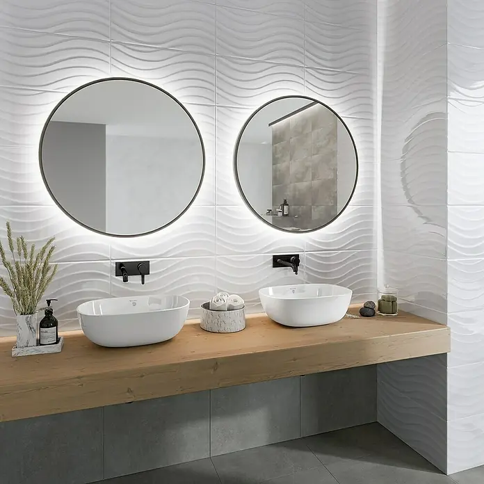 Ambiente by Palazzo Wandfliese Snowwhite Wave - 30 x 60 cm, Stärke: 9 mm, Weiß, Glänzend - Badezimmer mit zwei runden Spiegeln über Aufsatzwaschbecken auf einer Holzablage mit grauen Fliesen.