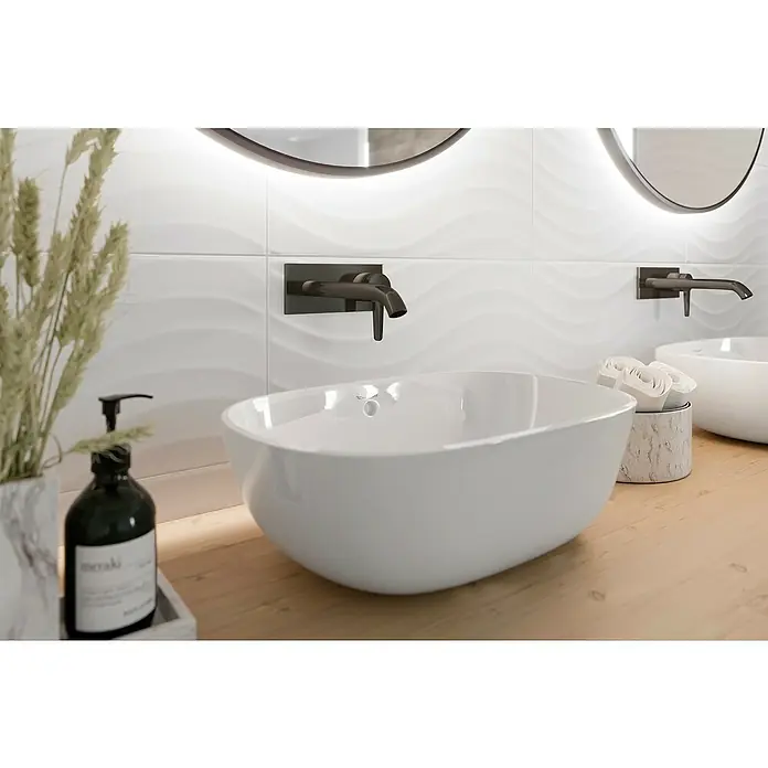 Ambiente by Palazzo Wandfliese Snowwhite Wave - 30 x 60 cm, Stärke: 9 mm, Weiß, Matt - Elegantes Badezimmerdesign mit einem modernen weißen Aufsatzwaschbecken und dunklen Armaturen vor strukturierten weißen Fliesen.