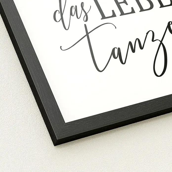 ProArt Bild Slim Scandic - Tanzen, B x H: 33 x 33 cm - Gerahmtes Bild mit schwarzem Holzrahmen und kalligrafischem Text „das LEBEN tanz“ auf weiß, an einer texturierten Wand.