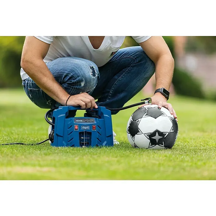 Scheppach Kompressor Air Force 5 - Max. Druck: 8 bar - Ein Mann hockt auf Rasen und pumpt einen Fußball mit einem blauen Scheppach-Luftkompressor auf, der auf dem Rasen steht.