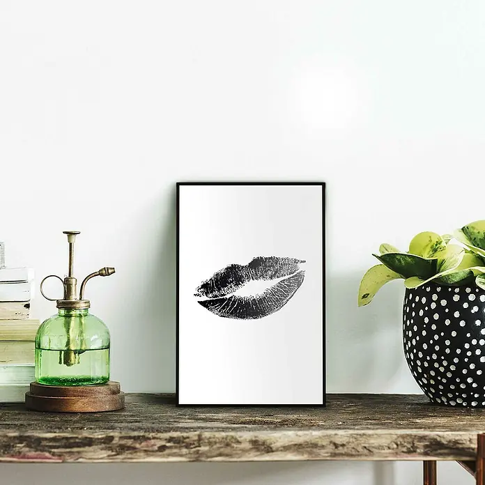 Reinders Bild Slim Frame Black - Hot Lips, B x H: 20 x 30 cm - Ein minimalistisches Bild mit einem Lippenabdruck in Schwarzweiß, gerahmt und auf einem Tisch ausgestellt. Dekorative Elemente umgeben das Kunstwerk.