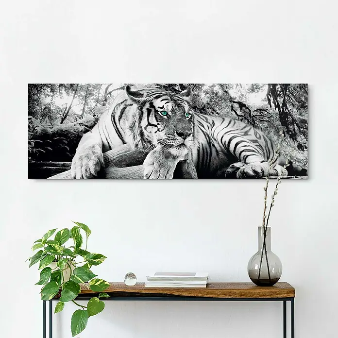 Reinders Holzbild Deco Block - Tiger is Watching You, B x H: 118 x 40 cm - Ein Schwarz-Weiß-Tiger Wandbild mit grünen Augen, das über einem Sideboard mit Dekoration und Pflanzen hängt.