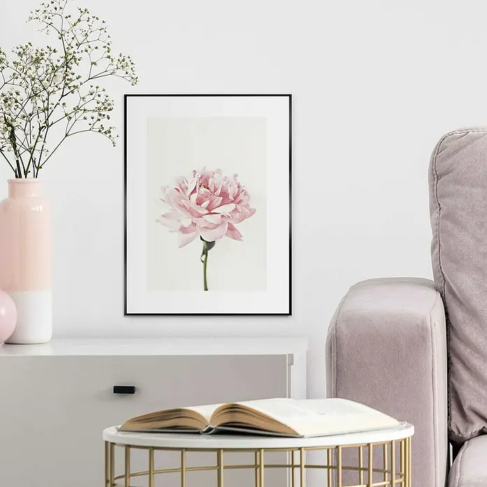 Reinders Bild Slim Frame Black - Pink Rose, B x H: 30 x 40 cm - Ein gerahmtes Rosenbild hängt an einer Wand über einem Schrank, neben einem Sofa und einem Tisch mit einem Buch.