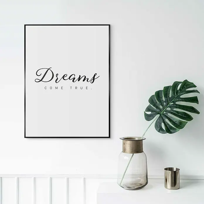 Reinders Bild Slim Frame Black - Dreams Come True, B x H: 30 x 40 cm - Ein gerahmtes Wandbild mit der Aufschrift „Dreams come true“ hängt über einem Tisch mit einer Vase und einer Monstera-Pflanze.
