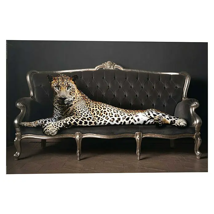 Reinders Decopanel - Panther Pose, B x H: 90 x 60 cm - Elegante Aufnahme eines Leoparden, der entspannt auf einem luxuriösen Sofa liegt, das mit silbernen Akzenten und dunklem, gestepptem Stoff versehen ist.