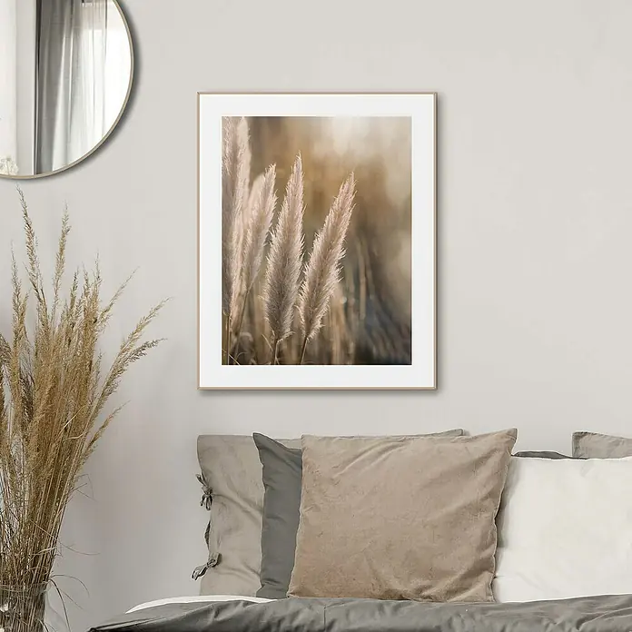 Reinders Bild Slim Frame Wood - Sunset Grasses, B x H: 40 x 50 cm - Ein gerahmtes Bild von Pampasgras hängt über einem Bett mit Kissen, ergänzt durch einen Spiegel und eine Vase mit Trockenblumen.
