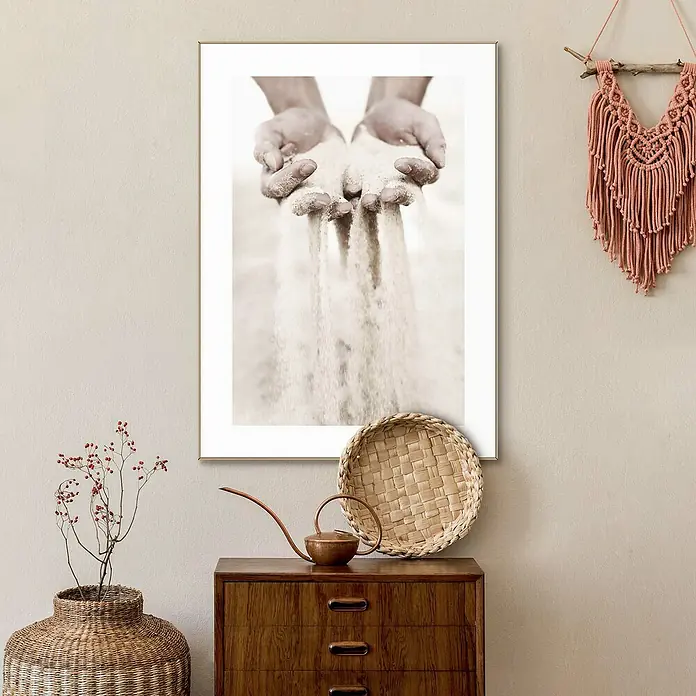Reinders Bild Slim Frame Wood - Hands in Sand, B x H: 50 x 70 cm - Ein dekoratives Foto mit Händen, die Sand halten, hängt über einer Holzkommode mit Dekorationen, die eine gemütliche Atmosphäre schaffen.