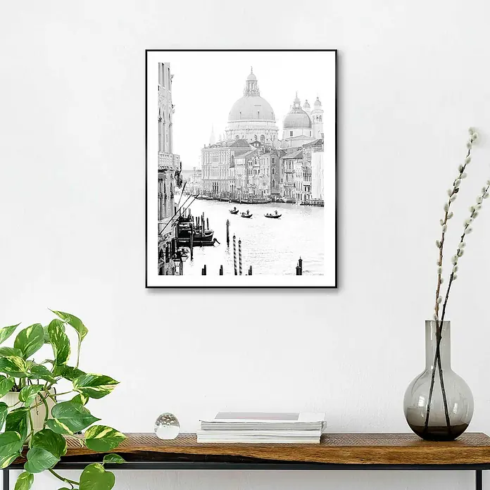 Reinders Bild Slim Frame Black - Classic Venice, B x H: 40 x 50 cm - Ein gerahmtes Schwarz-Weiß-Foto von Venedig hängt an einer weißen Wand über einem Holztisch. Das Bild fängt die ikonische Architektur und Kanäle ein.