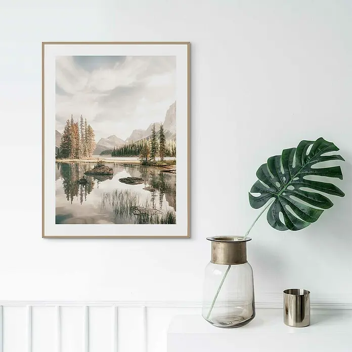 Reinders Bild Slim Frame Wood - Spirit Island, B x H: 30 x 40 cm - Ein gerahmtes Bild mit einer Berglandschaft am See hängt an einer weißen Wand über einem weißen Regal mit einer Vase und Dekoration.