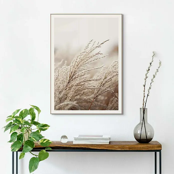 Reinders Bild Slim Frame Wood - Field Grass, B x H: 50 x 70 cm - Wandbild mit dem Motiv von Gräsern in sanften Farben, gerahmt und über einem Holztisch mit Deko-Elementen platziert.