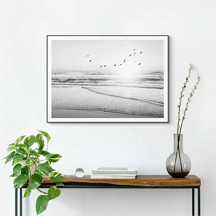Reinders Bild Slim Frame Black - Beach Serenity, B x H: 70 x 50 cm - Schwarzes gerahmtes Strandbild hängt über einem Holztisch mit Dekorationen, darunter eine Pflanze und eine Glasvase.