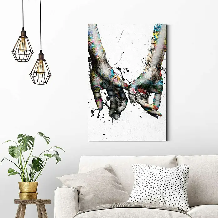 Reinders Decopanel - Pinkies Colour, B x H: 60 x 90 cm - Wandbild mit einem Motiv von zwei Händen, die sich berühren, im Wohnzimmer über einem Sofa mit Kissen.
