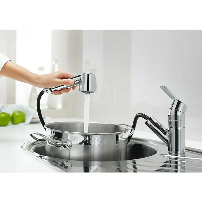 Roca Mitos Grifo de cocina - Extensible, Cromo, Brillante - Una mano llena una olla de acero inoxidable con un moderno grifo de cocina cromado con rociador extraíble en una cocina luminosa.