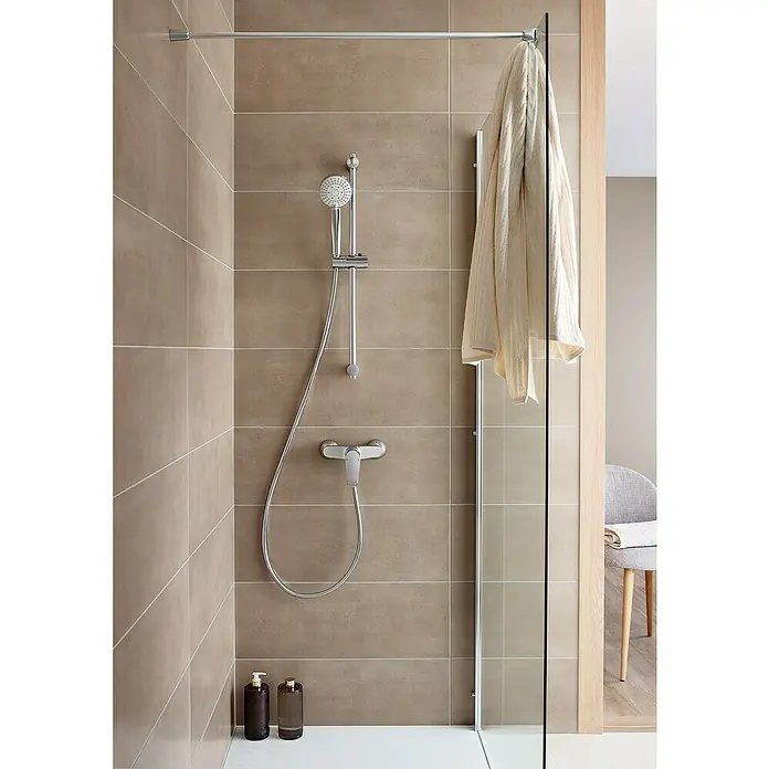Roca Eos-N Grifo monomando de ducha - Cromo, Brillante - Zona de ducha con accesorios plateados y cabezal de ducha, con una toalla colgada sobre una mampara de cristal.