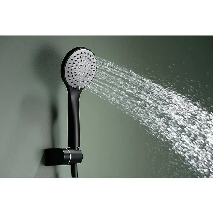 Imex Ural Grifo monomando de bañera - Negro, Mate - Primer plano de un moderno cabezal de ducha negro y redondo con agua que fluye sobre un fondo verde sereno.