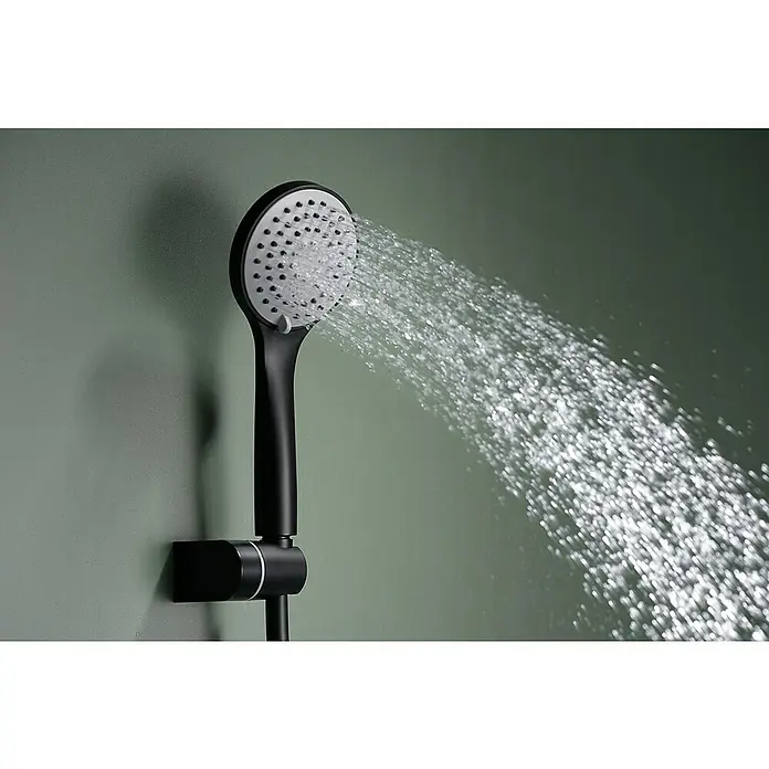 Imex Ural Grifo monomando de bañera - Negro, Mate - Primer plano de un moderno cabezal de ducha negro mate con interior blanco y un fuerte chorro de agua, mostrado contra un fondo verde.