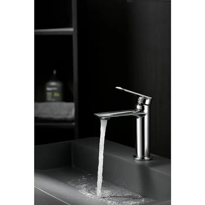 Imex Ural Grifo de lavabo - Cromo - Moderno grifo cromado con agua fluyendo hacia un lavabo oscuro y elegante, perfecto para diseños de baño con estilo.