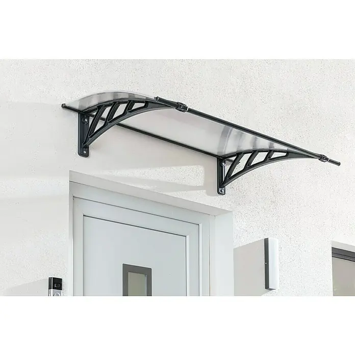 Palram – Canopia Pultvordach Apus - 119 x 76 x 25 cm, Anthrazitgrau - Das Bild zeigt ein modernes Türvordach mit schwarzem Rahmen und klarer Abdeckung, das über einer weißen Tür an einer strukturierten Wand montiert ist.