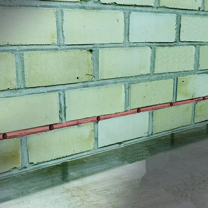 MEM Trockene Wand Fix & Fertig - 290 ml - Nahaufnahme einer Ziegelwand mit einer Kupferleitung, die horizontal verläuft und mit Bohrlöchern versehen ist.