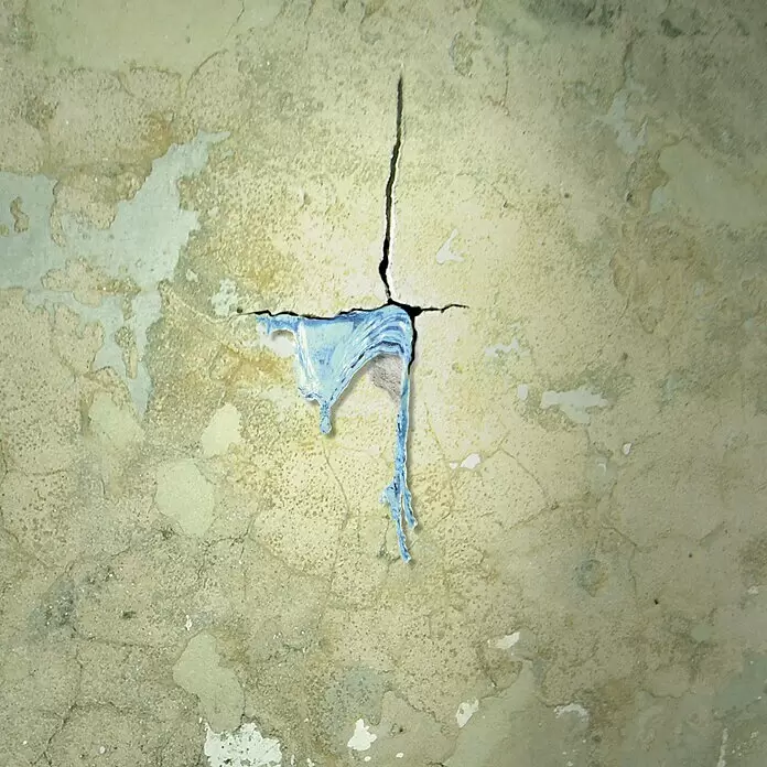 MEM Wasser-Stopp - 1 kg - Blau-transparente Substanz tritt aus einem kreuzförmigen Riss in einer strukturierten, beschädigten Wand aus.