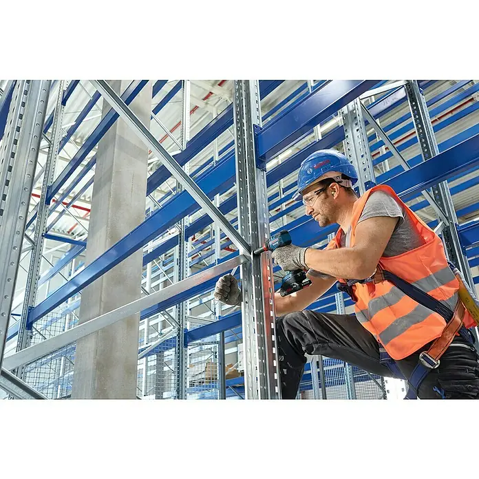 Bosch Professional AMPShare 18V Akku-Drehschlagschrauber GDX18V-200 - 18 V, 2 Akkus, 4 Ah, 200 Nm, Inkl. Koffer - Ein Handwerker mit einem Bosch Akku-Schlagschrauber bei der Arbeit in einem Lagerhaus. Er trägt Helm und Schutzweste.