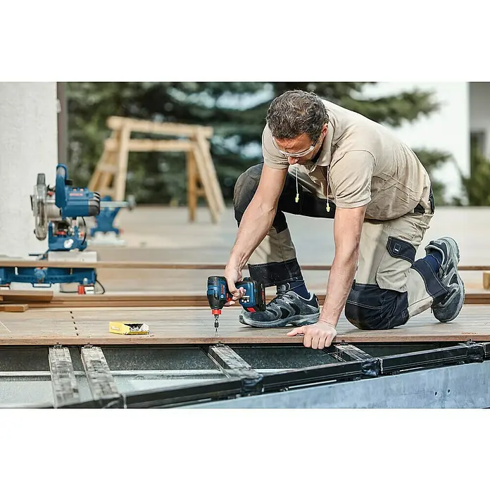 Bosch Professional AMPShare 18V Akku-Drehschlagschrauber GDX 18V-210 C - 18 V, Ohne Akku, 210 Nm, Mit Bluetooth-Modul - Handwerker mit einem Bosch Akku-Bohrschrauber beim Bau einer Holzterrasse, im Hintergrund eine blaue Säge.