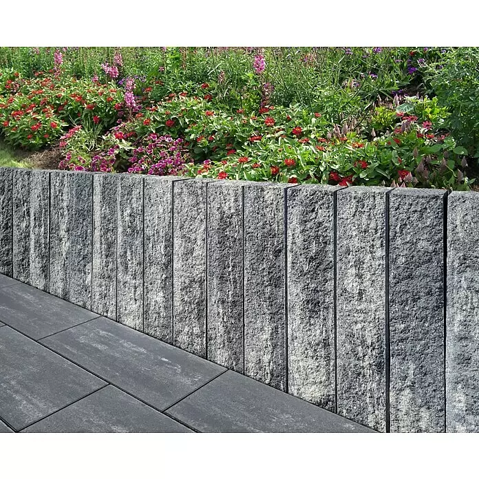 Diephaus Stamford Mauerstein - 30 x 10 x 10 cm, Schwarz/Weiß, Beton - Graue, texturierte Stützmauer trennt dunkelgraue Pflastersteine von einem bunten Blumenbeet.