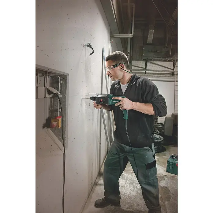 Metabo Elektro-Pendelhubstichsäge STEB 65 Quick - 600 /min - 3.000 /min, Max. Schnitttiefe in Holz: 65 mm, Anzahl Pendelhubstufen: 4 Stk. - Ein Mann bohrt mit einer Metabo-Bohrmaschine ein Loch in eine Betonwand, wobei er Sicherheitsbrille und Gehörschutz trägt.